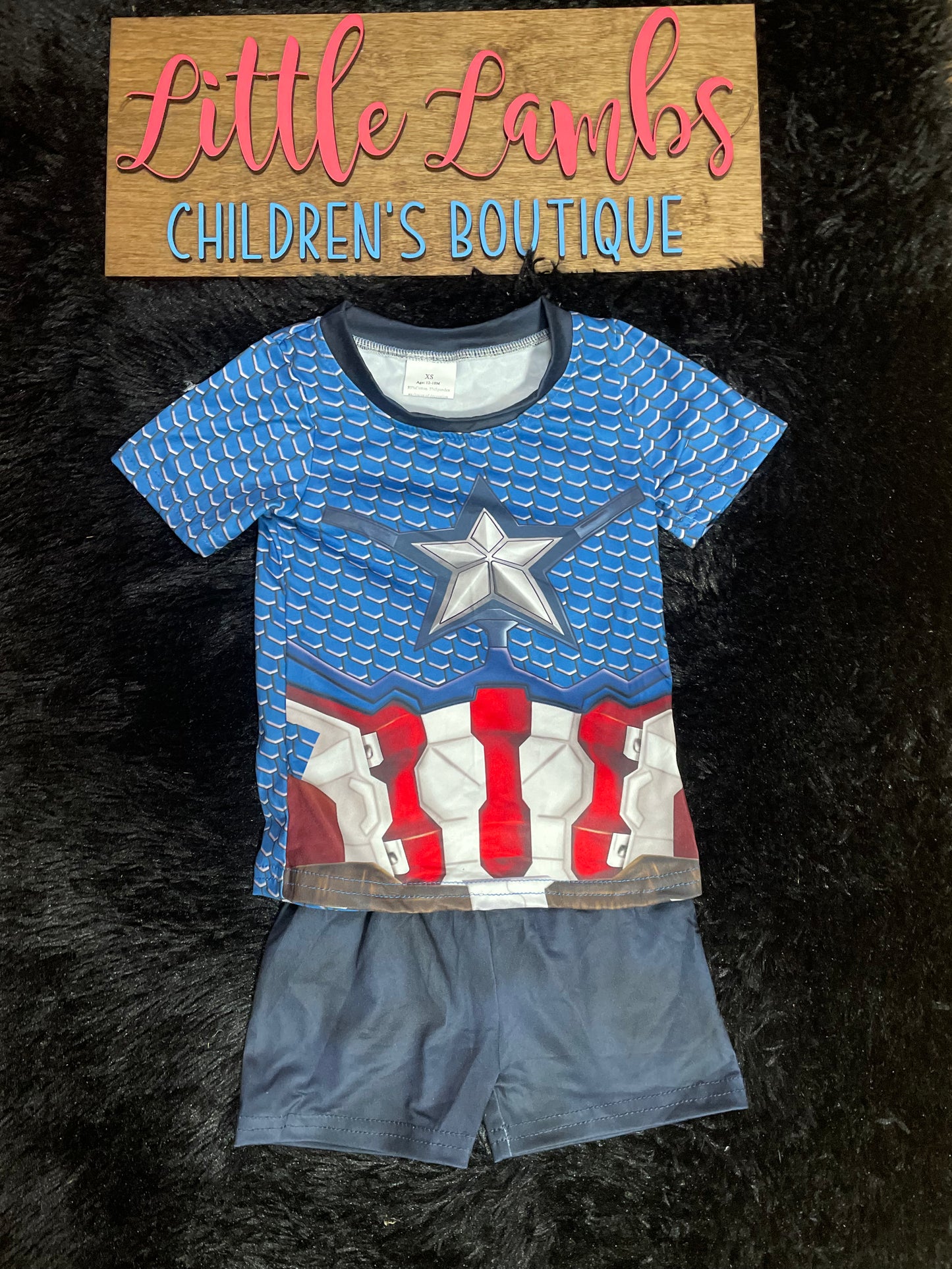 A short set for children featuring a Captain America themed shirt with blue and red colors and a matching pair of gray shorts with a Captain America logo on the shorts.